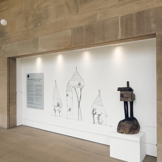 A carved wooden house displayed next to a series of large scale house drawings.