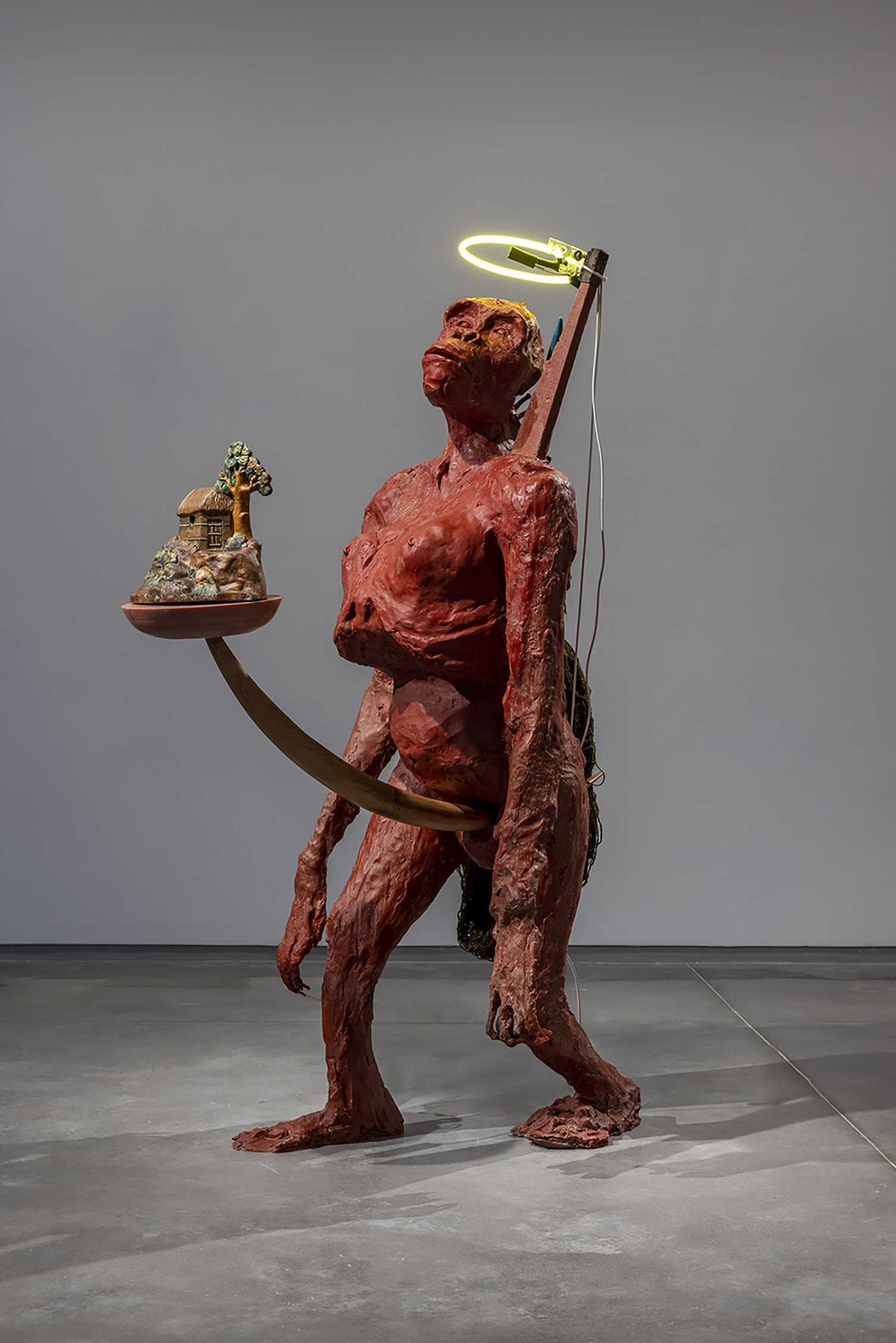 A red ape-like sculpture, with a glowing halo and a small house on a platform coming out of it's stomach.