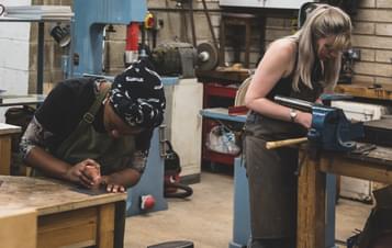 Two women working with carving tools in a workshop space