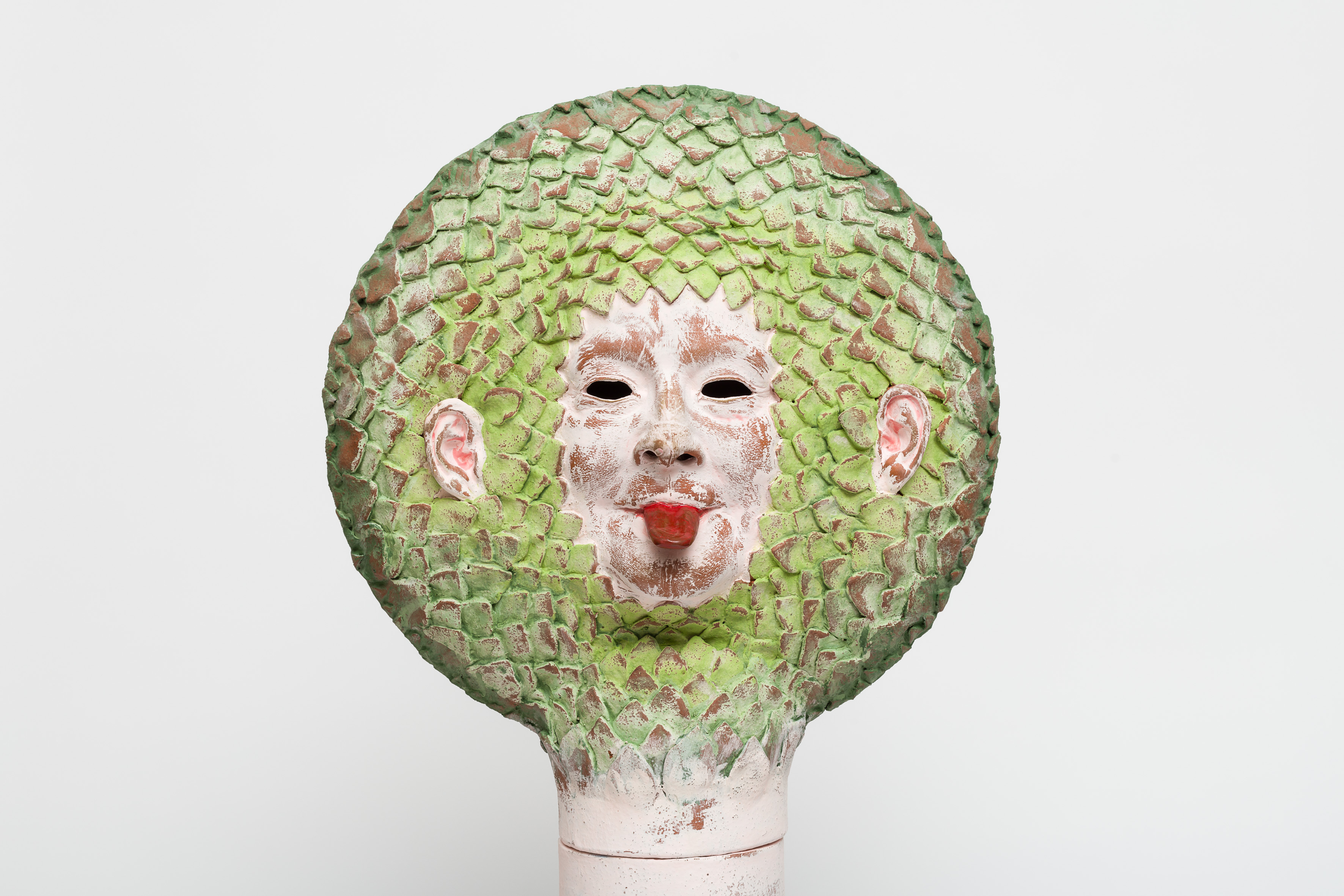A ceramic face with it's tongue out, with green leaf-like hair.