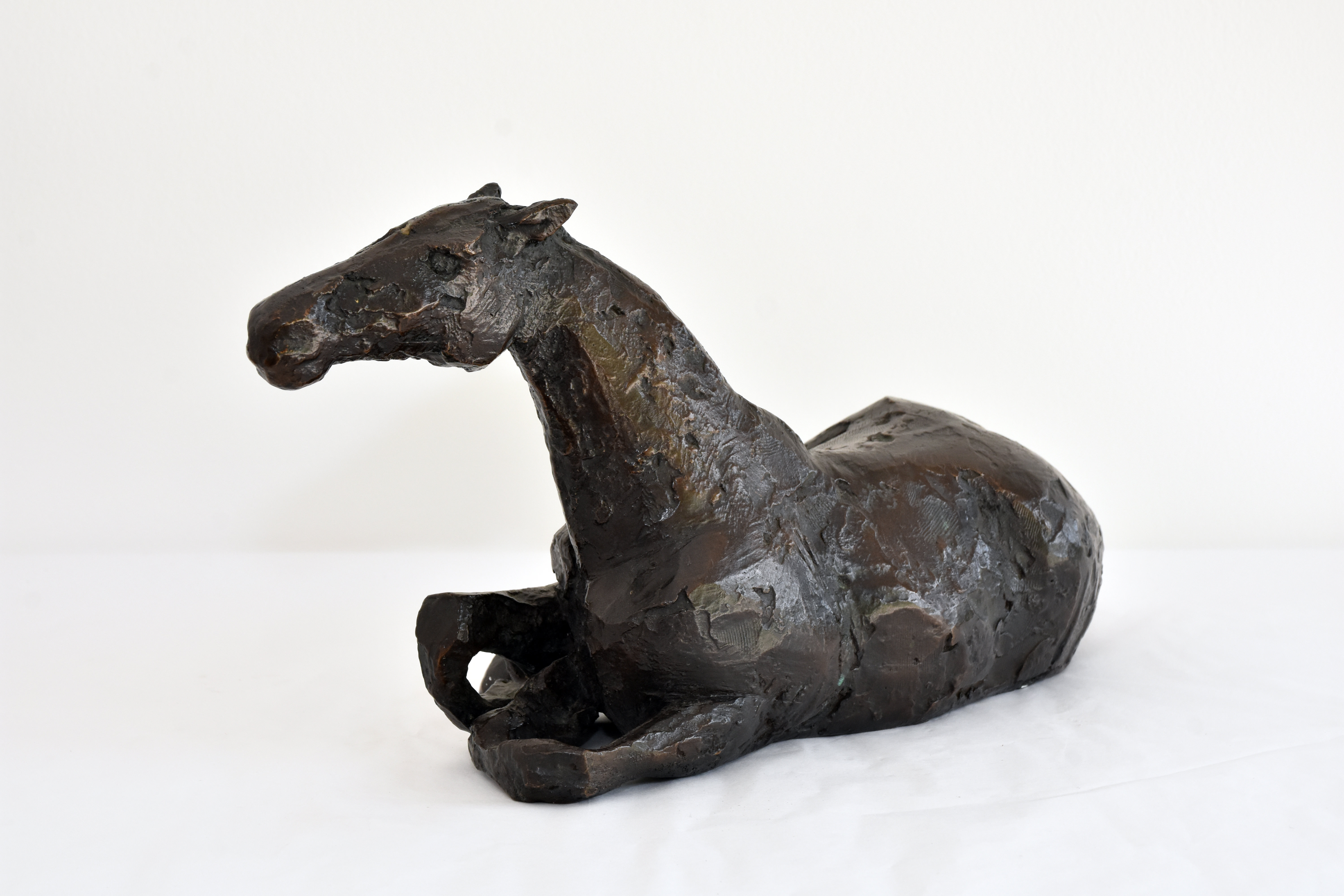A bronze sculpture of a horse lying down.