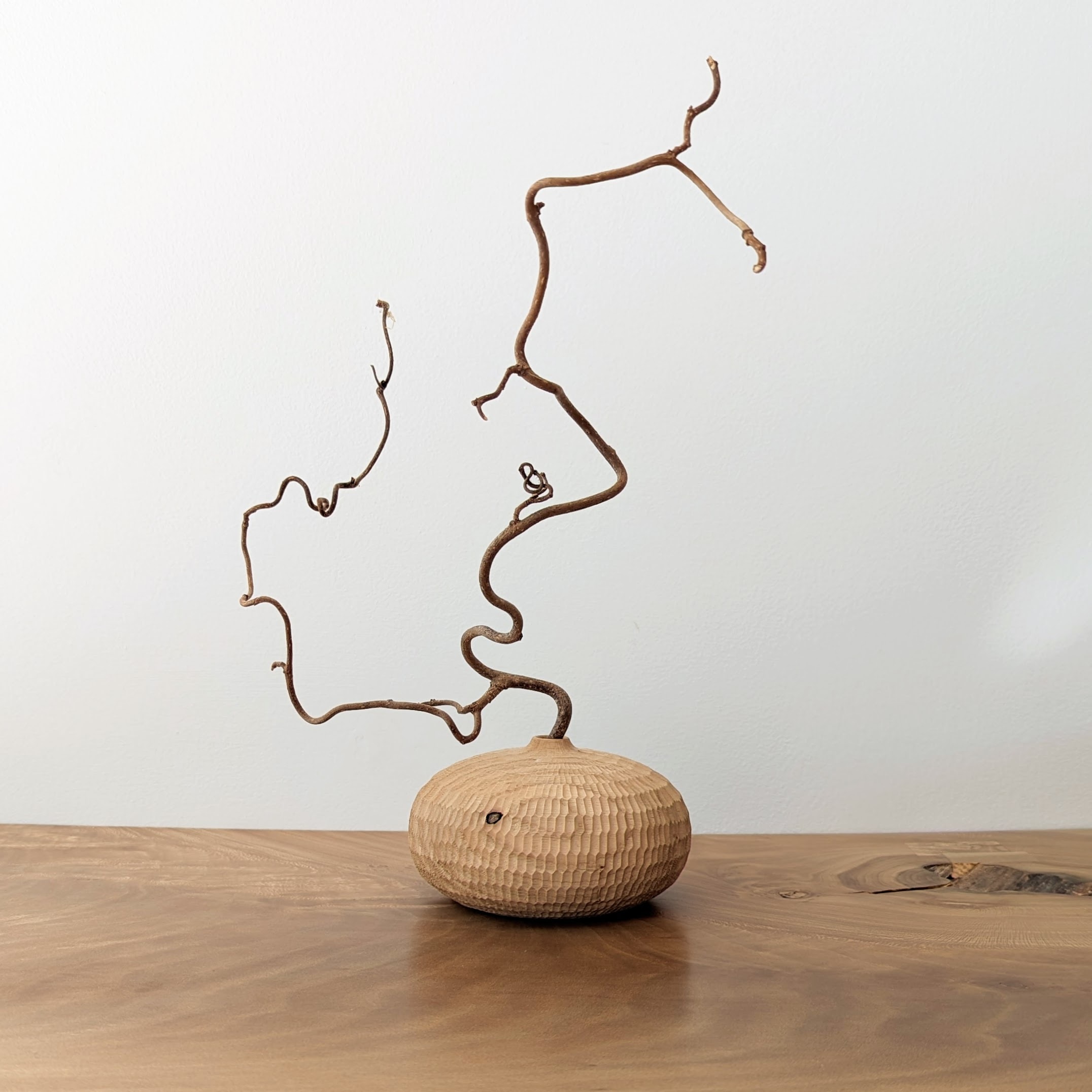 A carved wooden vessel with a twisted branch coming out of it.