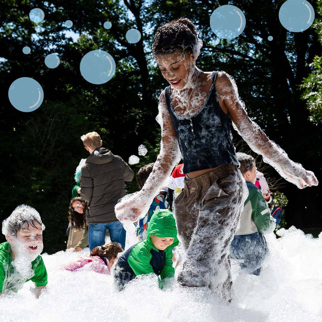 A group of mixed age children playing in a cloud of foam with cartoon bubbles overlay.