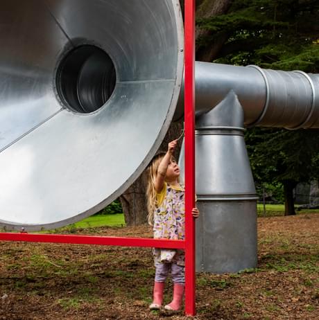 A child touching a giant silver tube with a stick
