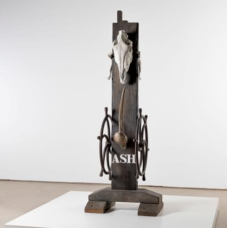 Sculpture reads ASH at its base and has an animal skull hung at the top.