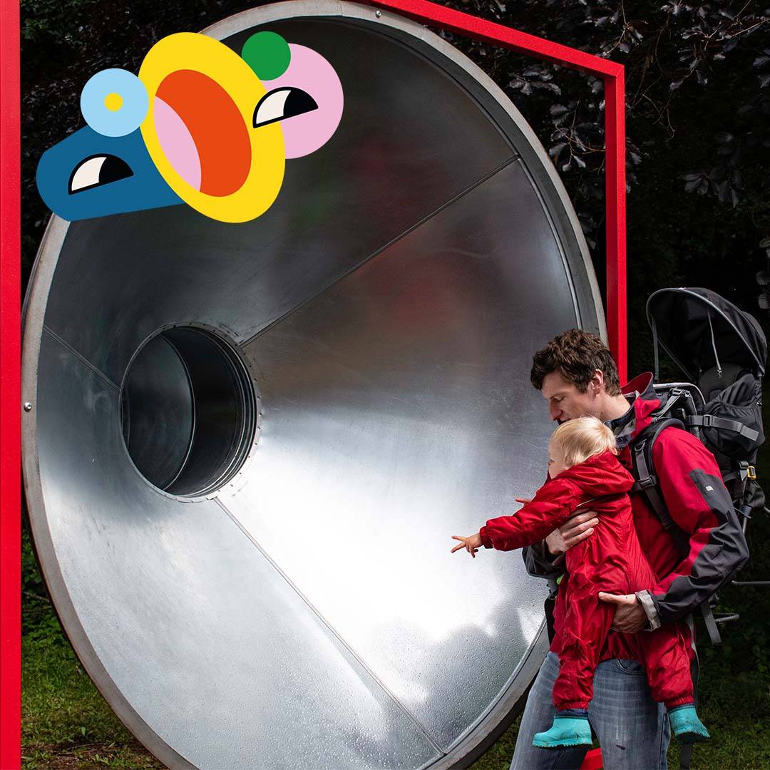 A man and baby looking into a giant silver tube, with cartoon face overlay