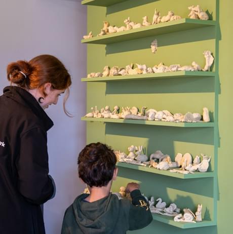 A child adding their wax animal to a self full of wax models