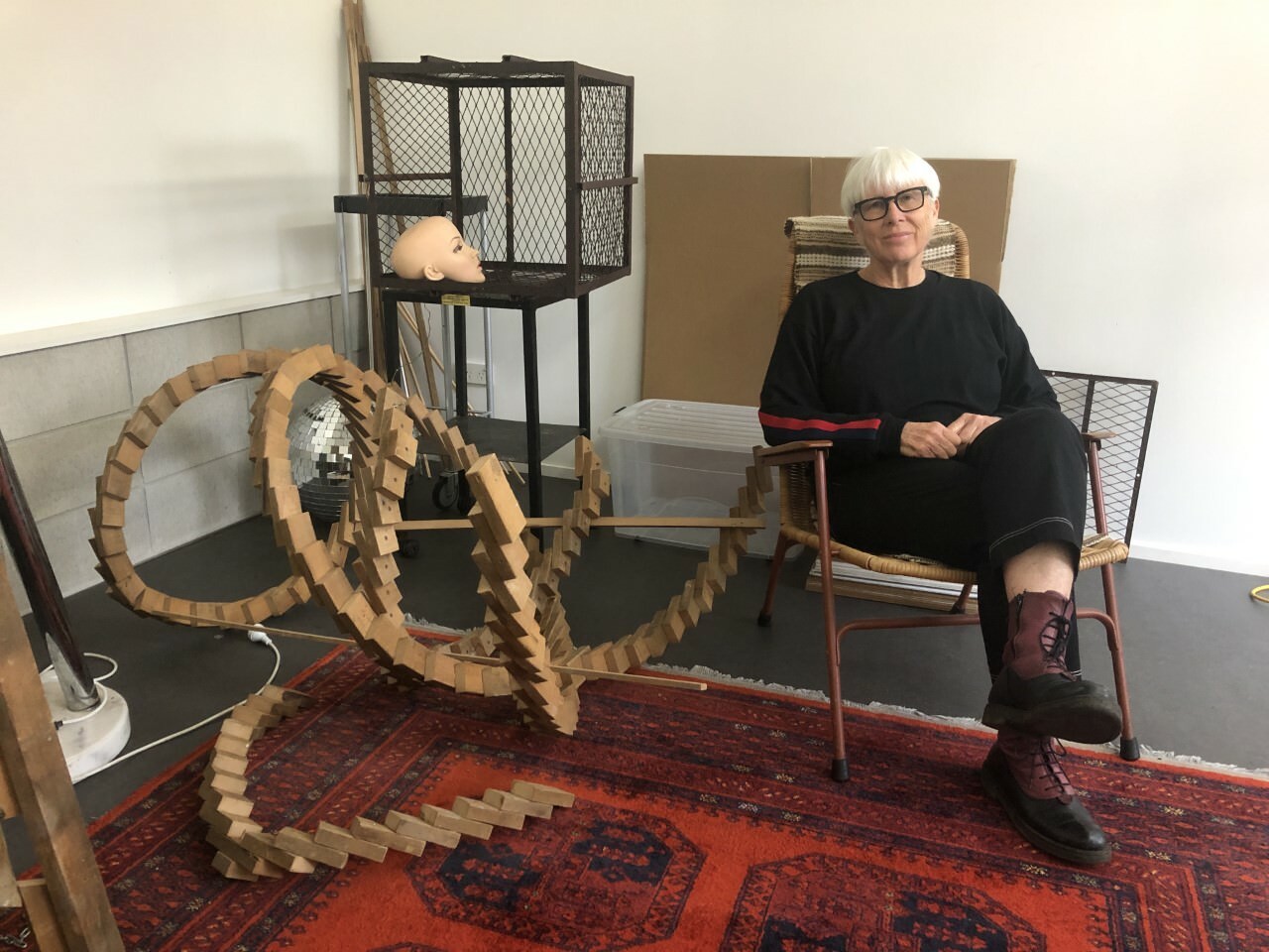 The artist Deborah Rundle sitting in a chair next to a wooden sculpture