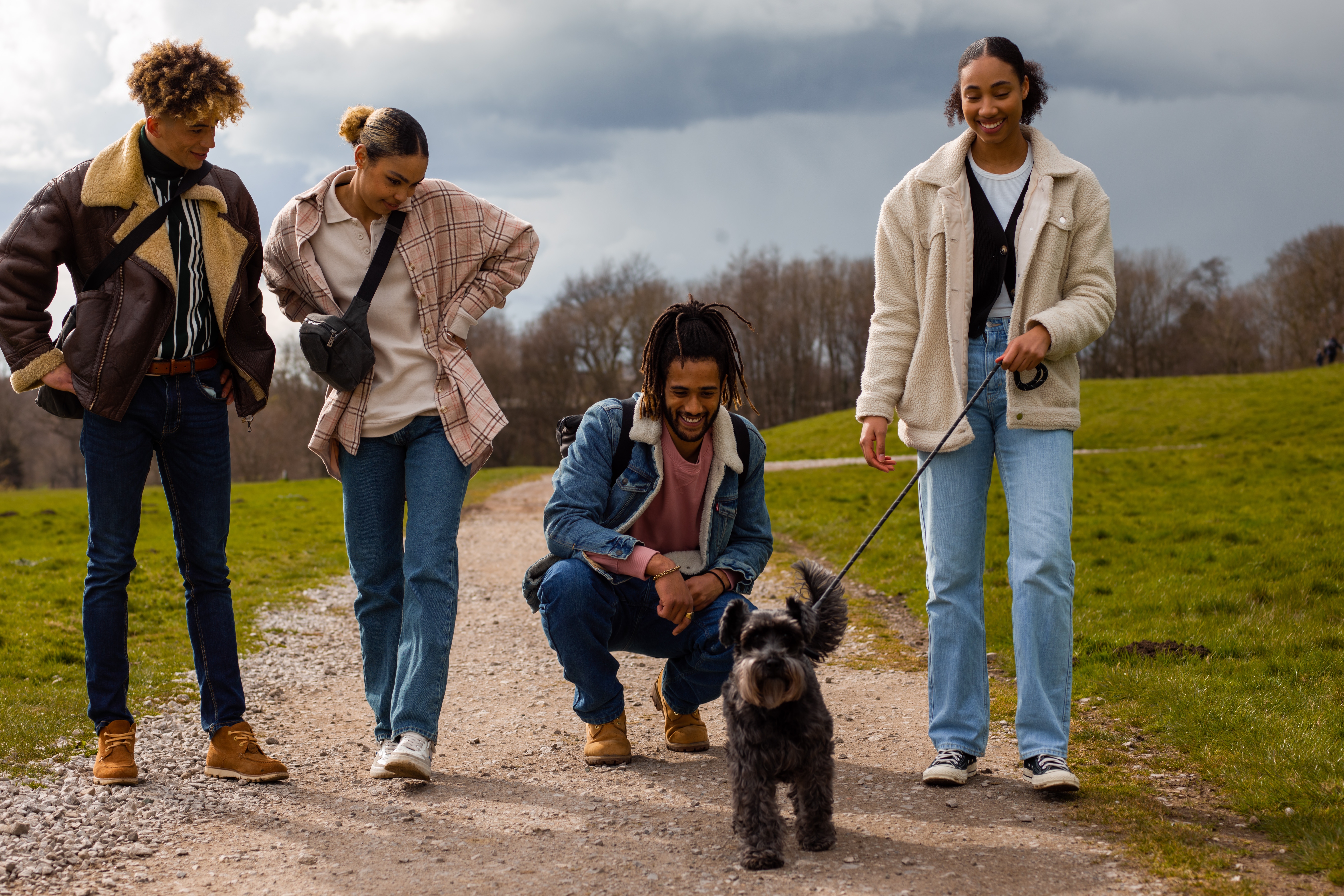 A group of 4 young people walking a small grey dog through the country park