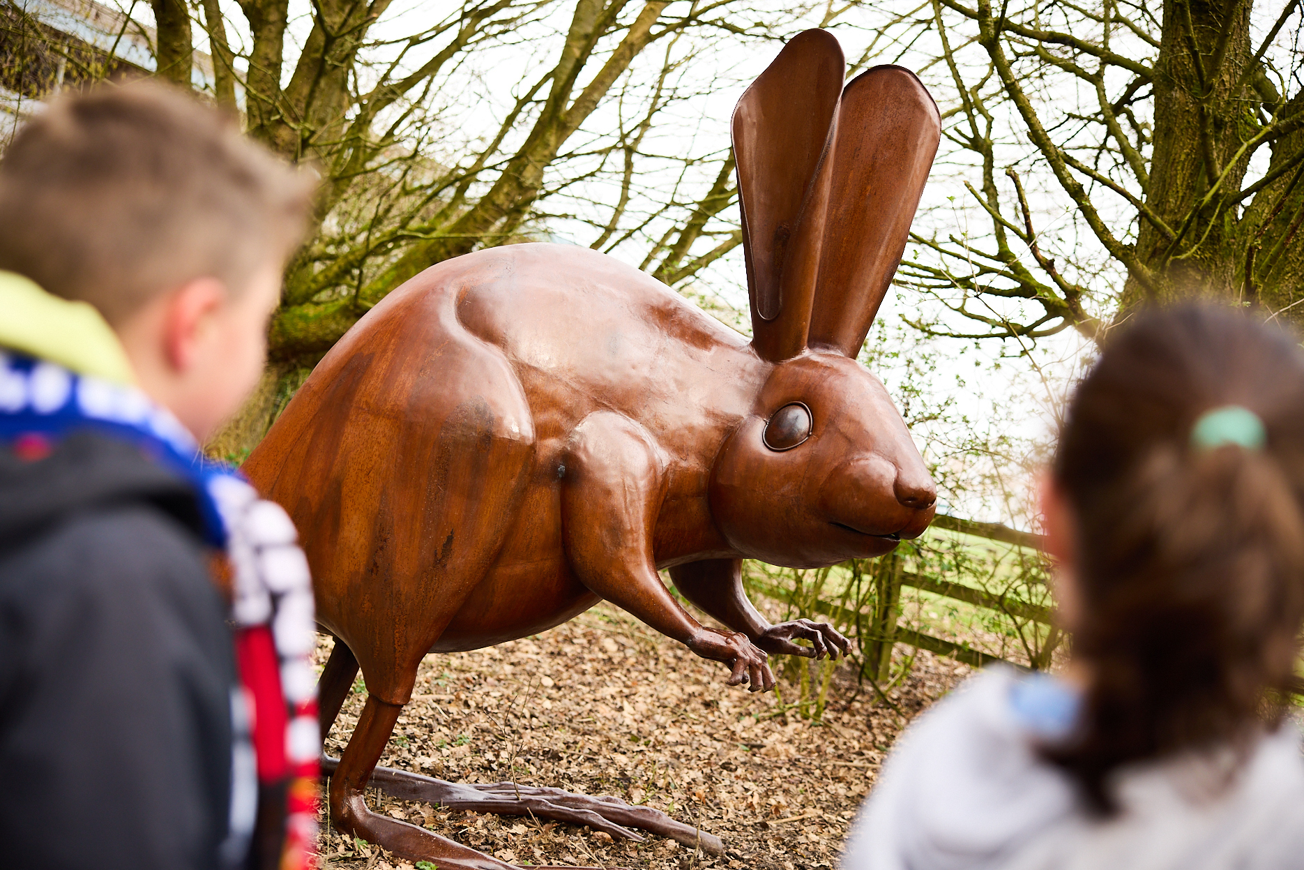 Two children looking at a bronze long-eared mouse sculpture outdoors