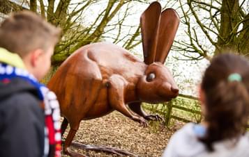 Two children looking at a bronze long-eared mouse sculpture outdoors