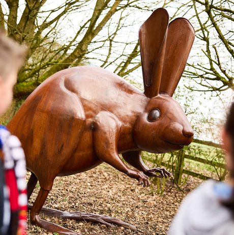 Two children looking at a bronze long-eared mouse sculpture outdoors