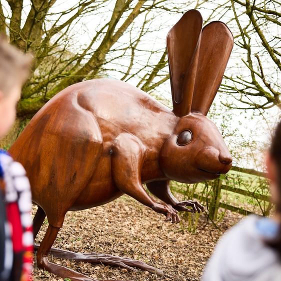 Two children looking at a bronze long-eared mouse sculpture outdoors