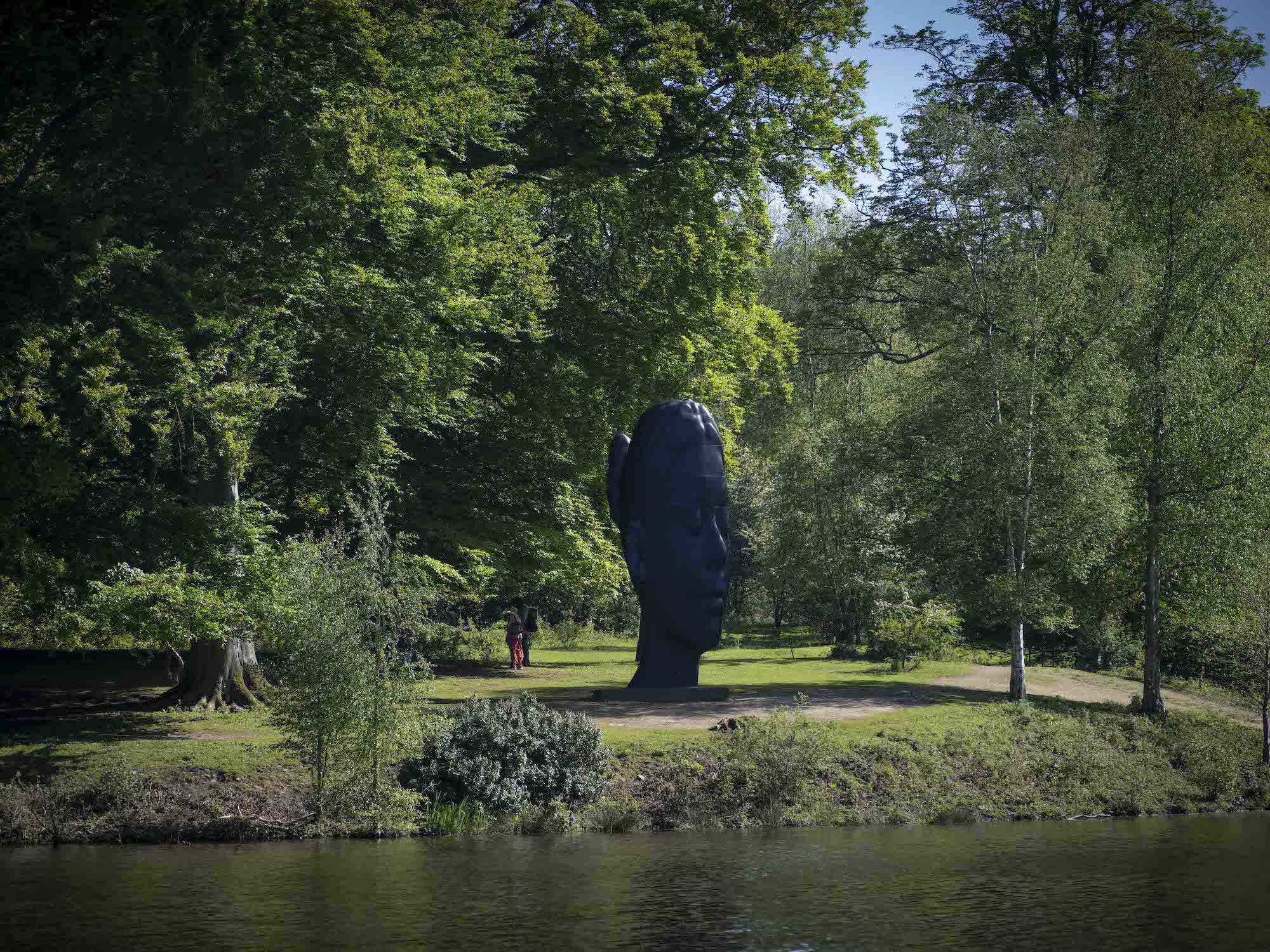 A sculpture of a girl's head flanked by trees, overlooking the lake.