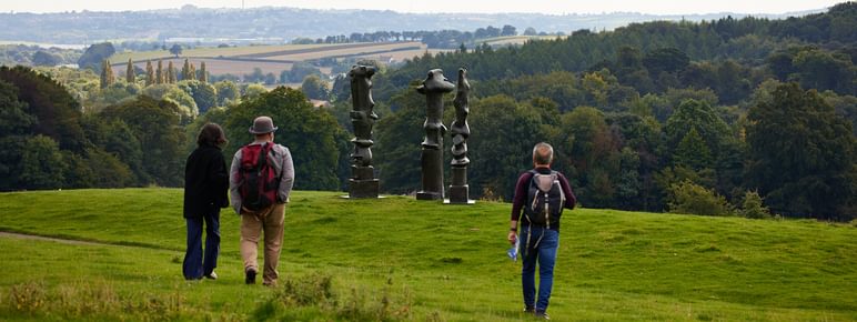 A group of people walking towards three tall thin sculptures on a hillside.