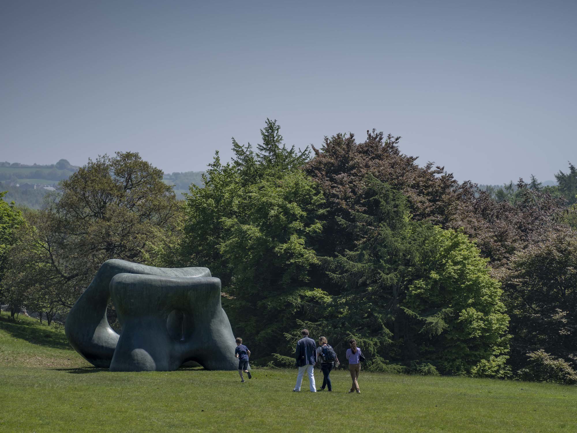 People walk across the grass in the country park towards a Henry Moore sculpture.
