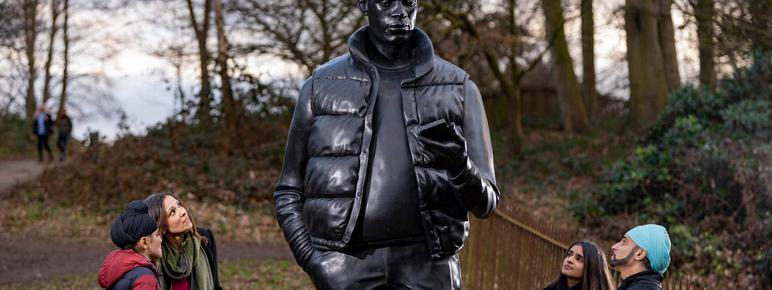 A family look up at a large sculpture of a man holding a mobile phone.