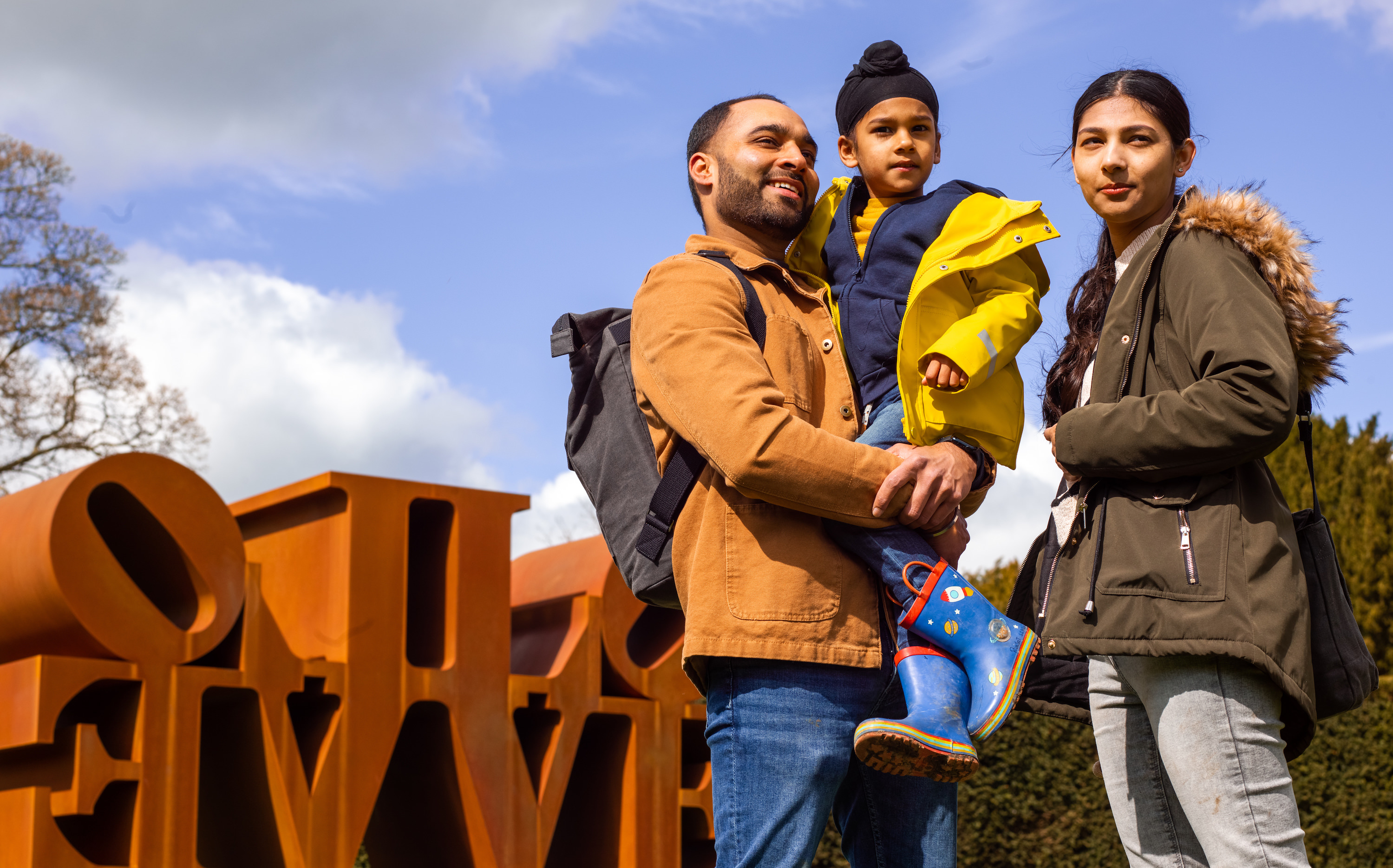 two adults and a child smiling in front of a Robert Indiana sculpture at YSP