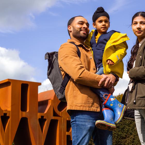 two adults and a child smiling in front of a Robert Indiana sculpture at YSP