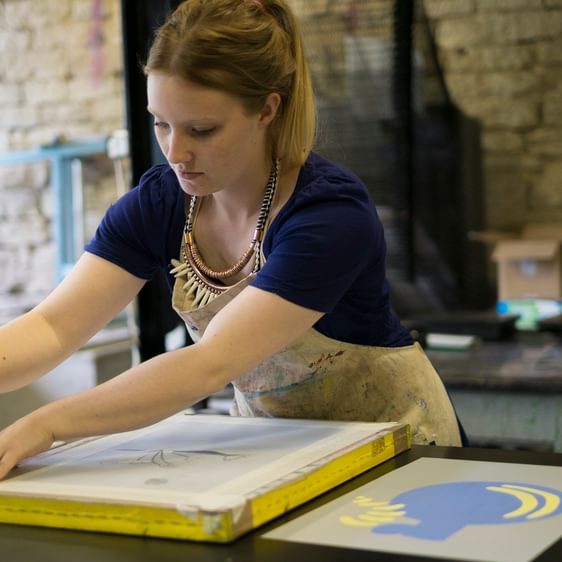 A woman wearing an apron preparing a screen printing screen