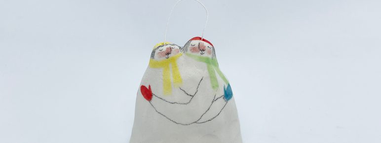 A porcelain bell ornament, painted to show a couple in scarves in an embrace.