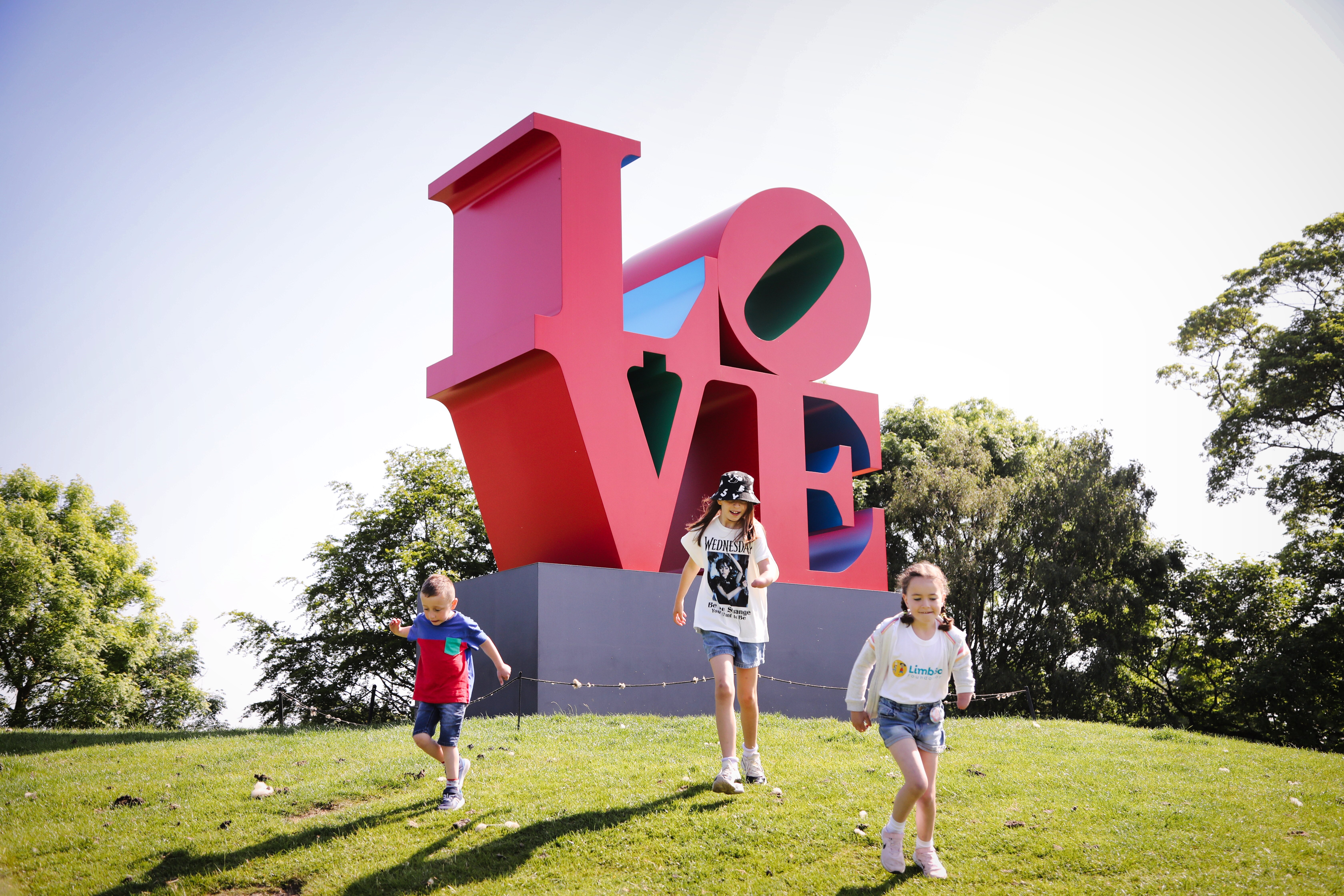 Children running down a hill in front of a large red LOVE sculpture by Robert Indiana