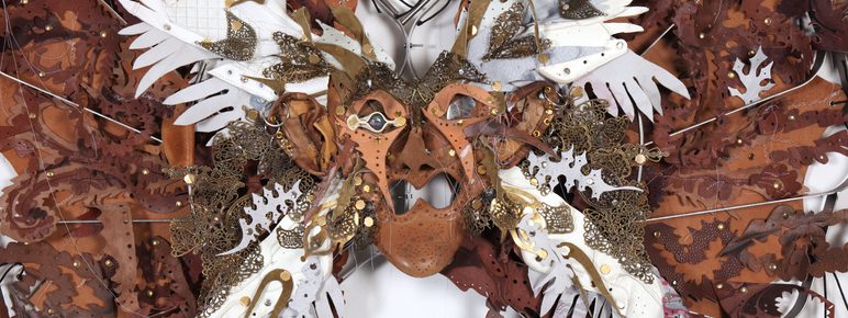 A striking wall art piece resembling a butterfly, crafted from various materials including metal, leather, and paper. The central mask features intricate details, with white and brown wings adorned with embellishments, creating a vibrant, textured display.