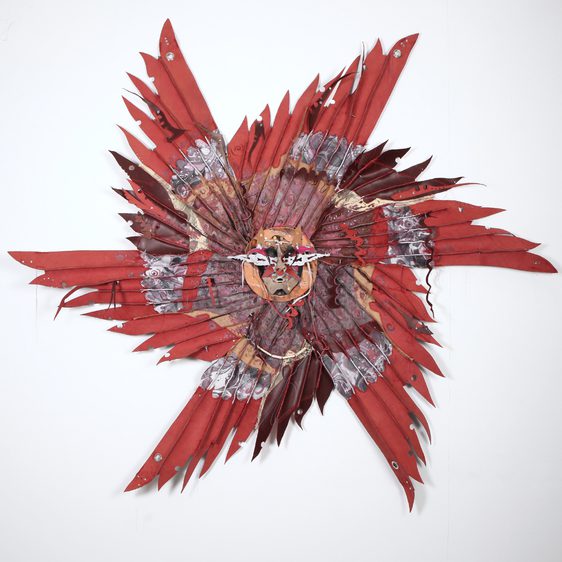 A vibrant, abstract wall sculpture featuring a central face surrounded by an array of red and brown feathers. The piece combines intricate patterns and textures, creating a striking visual impact against a plain white background.