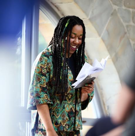 A black woman with braided hair smiling while reading from a booklet