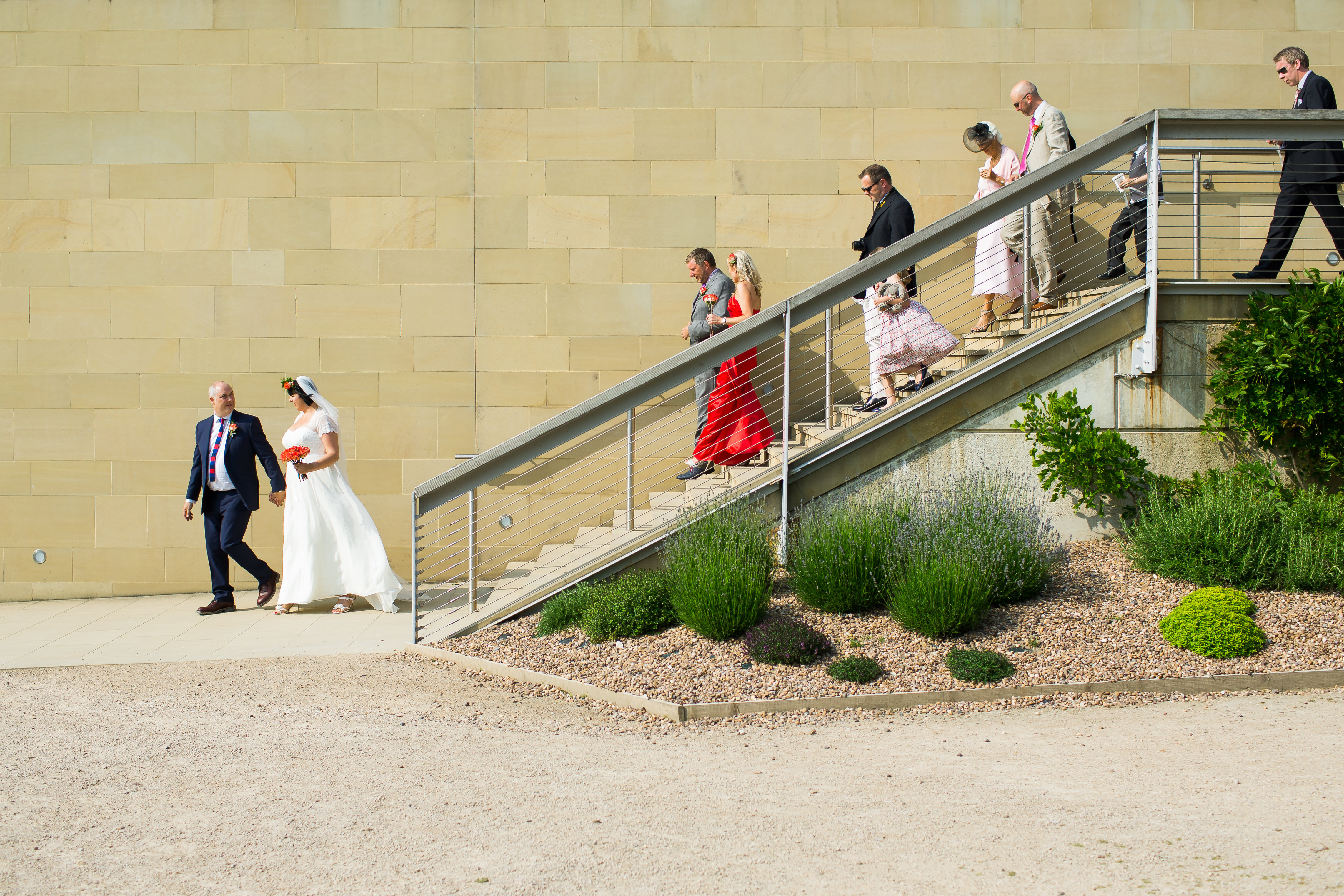 A wedding part, led by the bride and groom, walking down steps outside the Underground Gallery at YSP