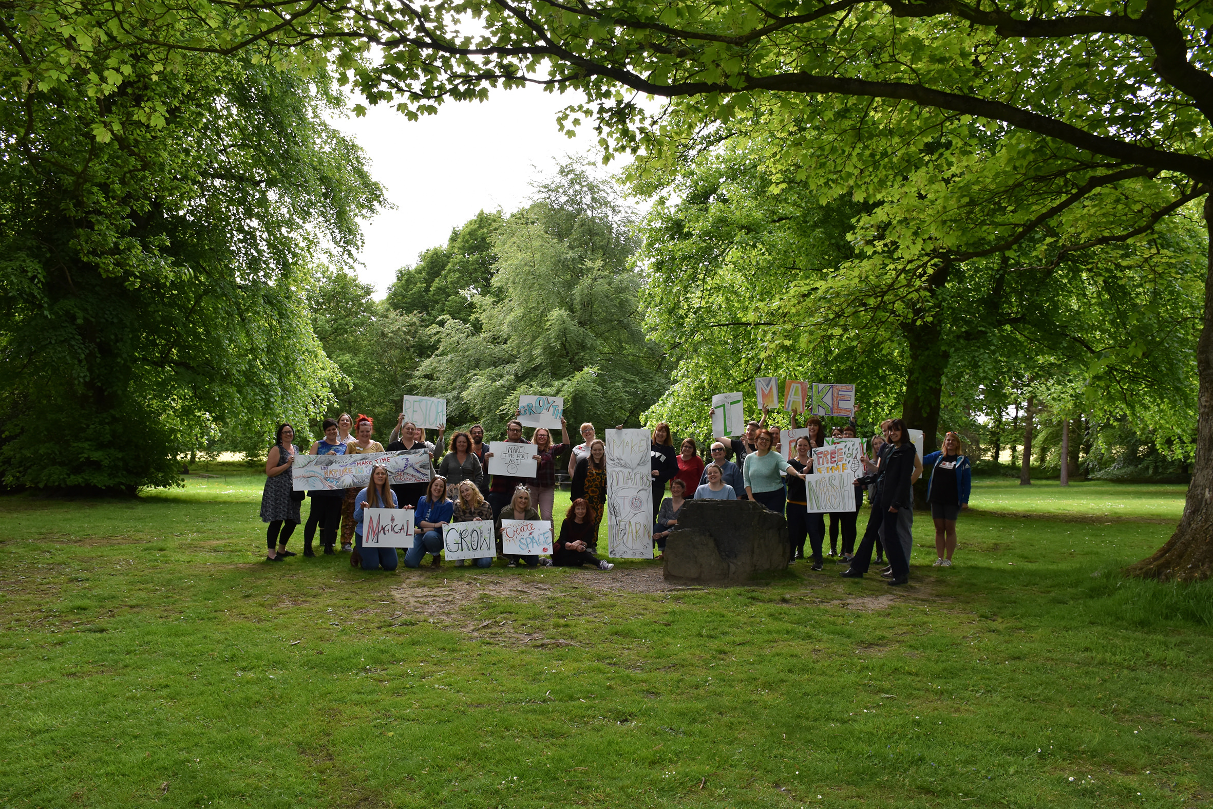 A large group of people holding hand decorated banners under the trees at YSP.