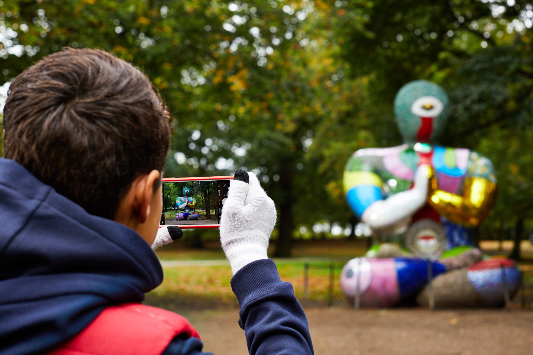 A child photographing a colourful sculpture on a mobile phone.
