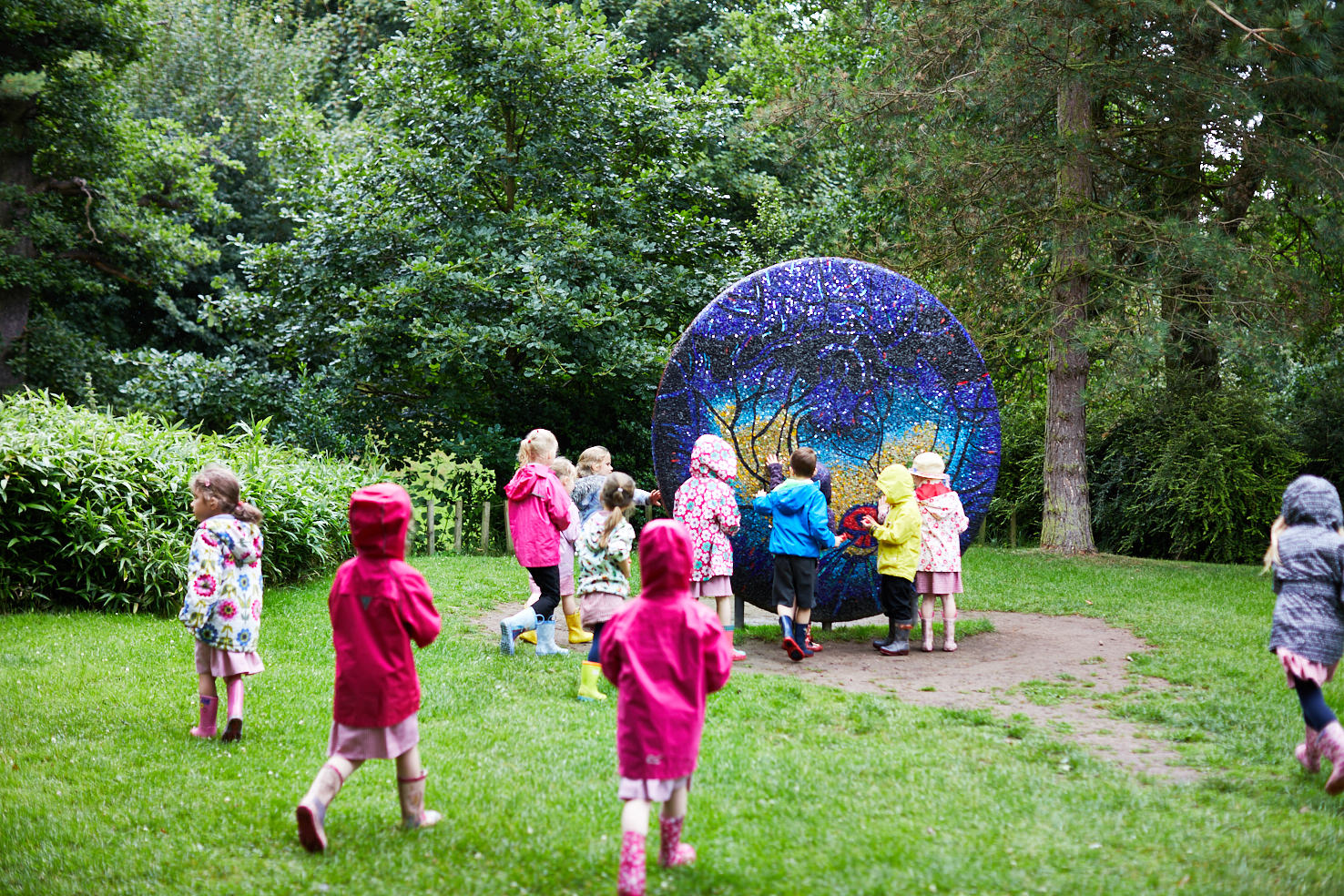 A large group of young children admiring and touching a textured sculpture in the rain.