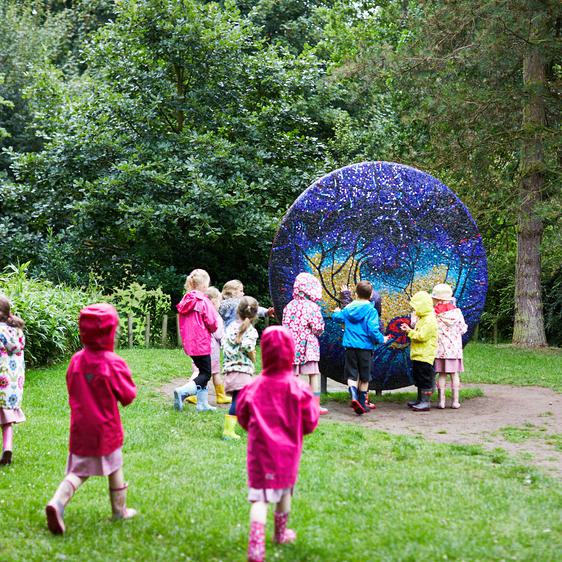 A large group of young children admiring and touching a textured sculpture in the rain.