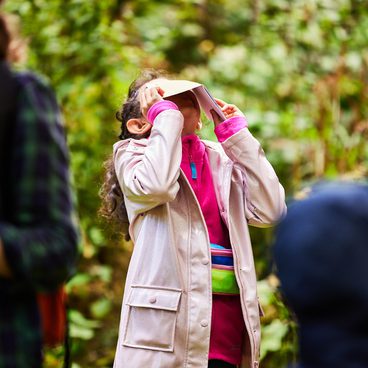 A child tilting their head back, with a sketchbook covering their face.