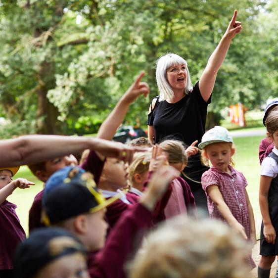 A group of young school children with two adults pointing into the sky.