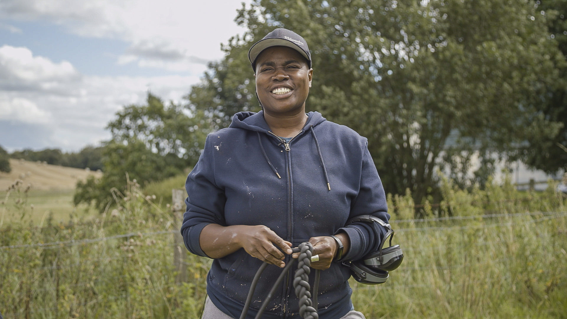 A black woman wearing a blue hoody, standing in a field at YSP