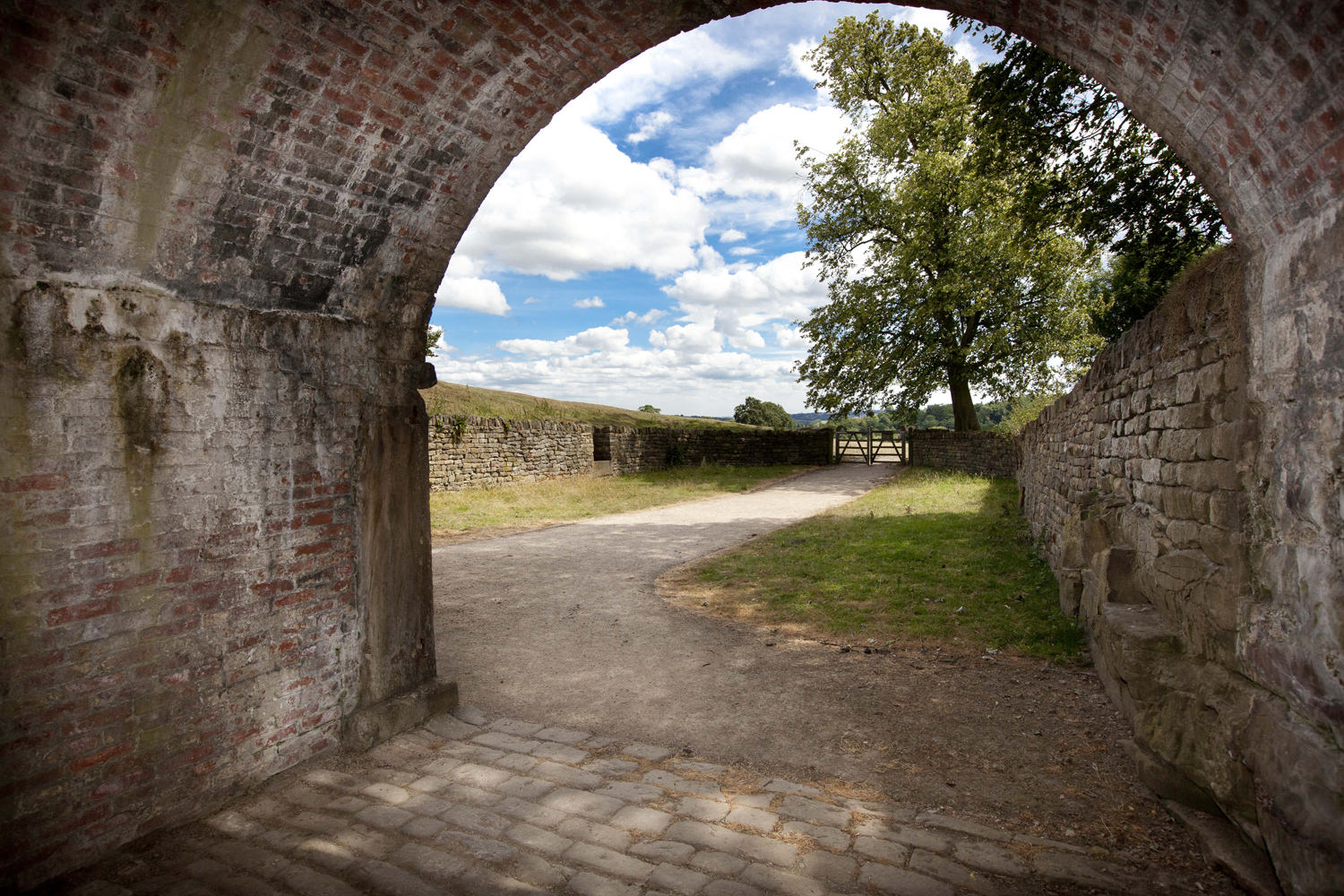 The view from a brick archway out over the countryside with a blue, cloudy sky