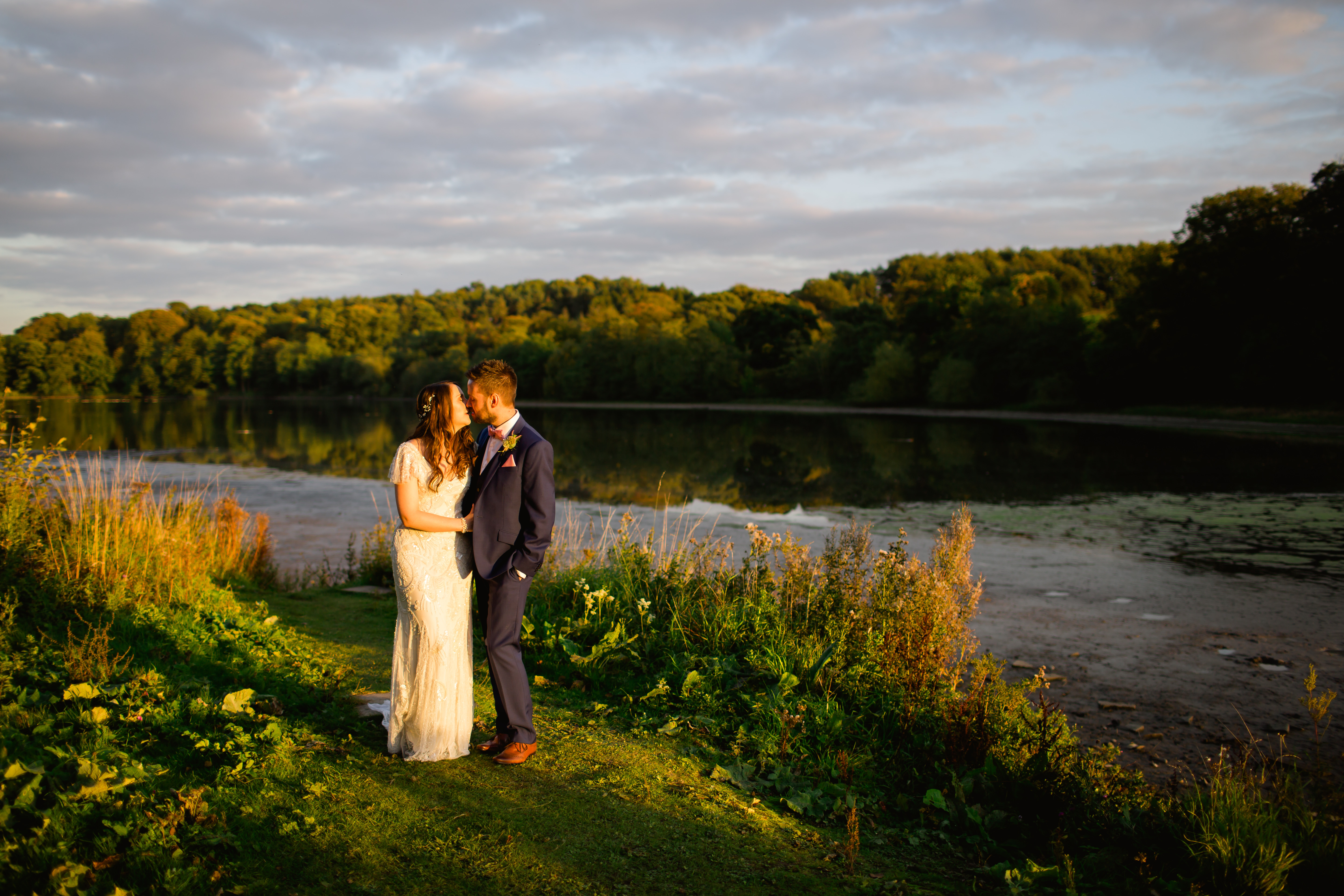 A bride and groom standing in front of a lake