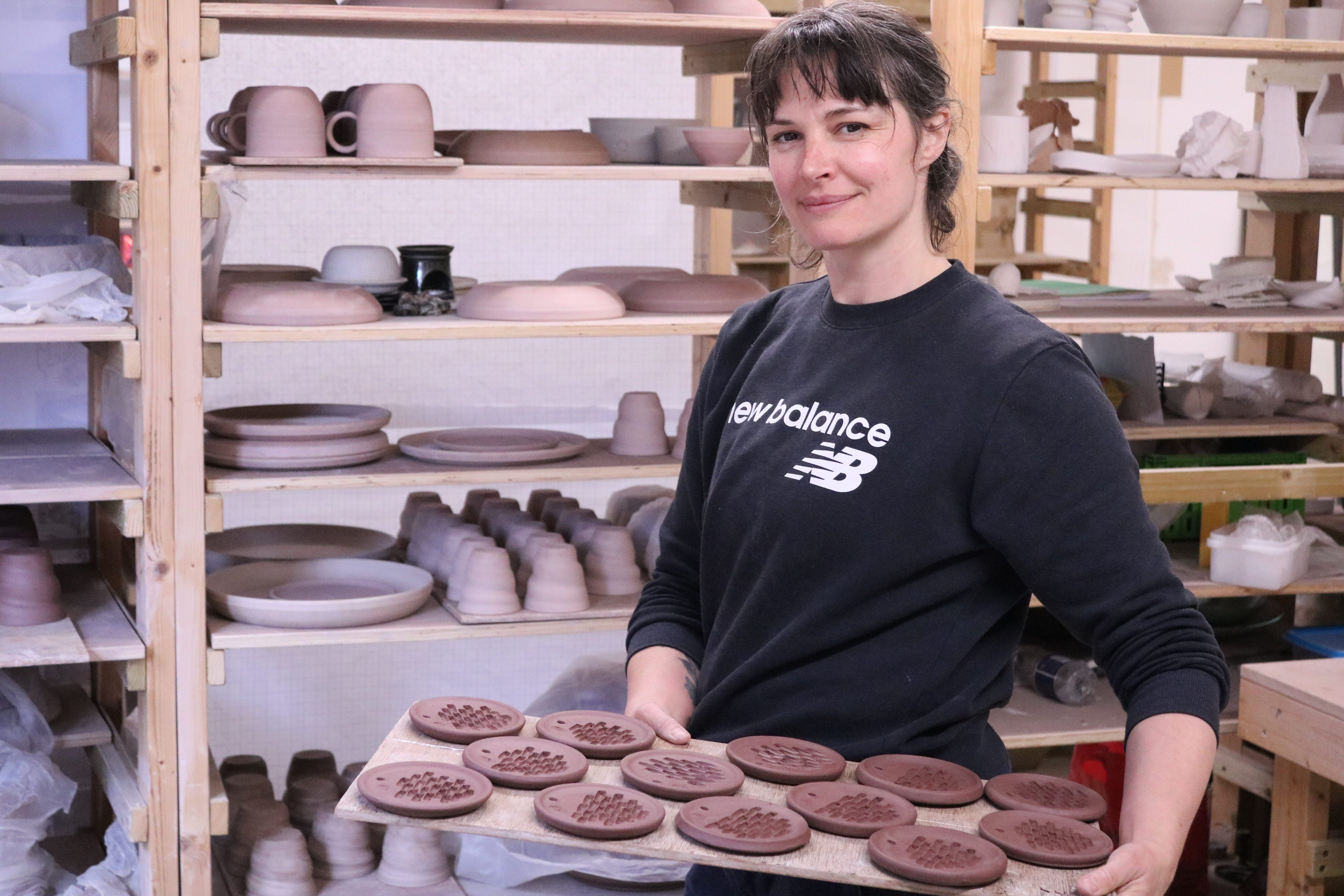 A woman with brown hair, holding a tray of unfired ceramics