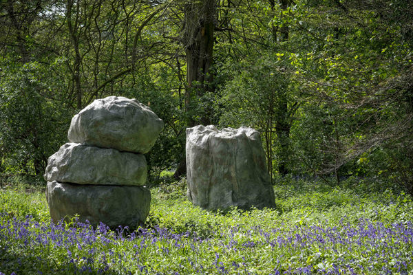 Two grey boulder-like sculptures surrounded by bluebells