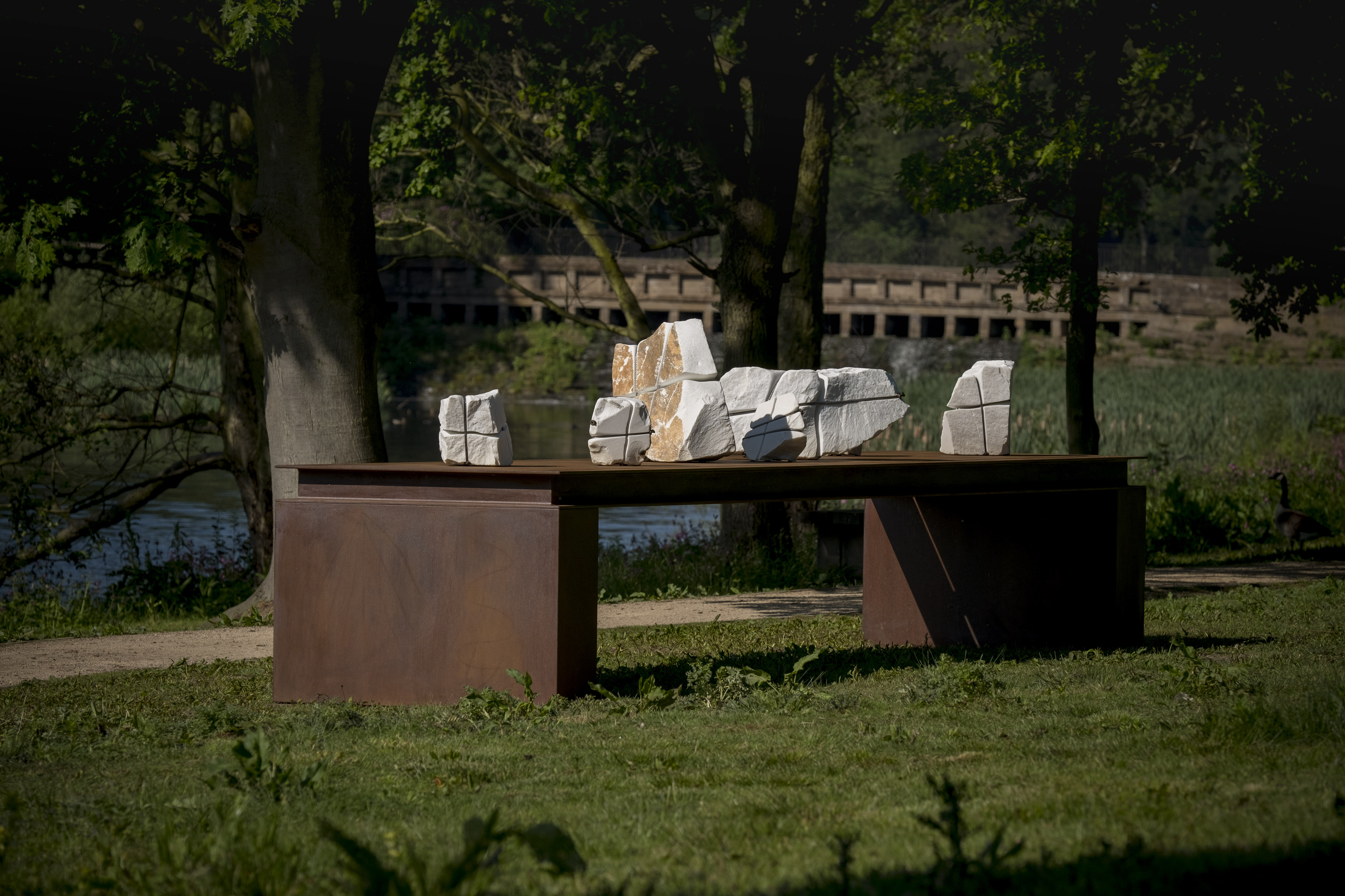 A bronze table structure with white marble pieces wrapped in wire on top. The cascade bridge is in the background.