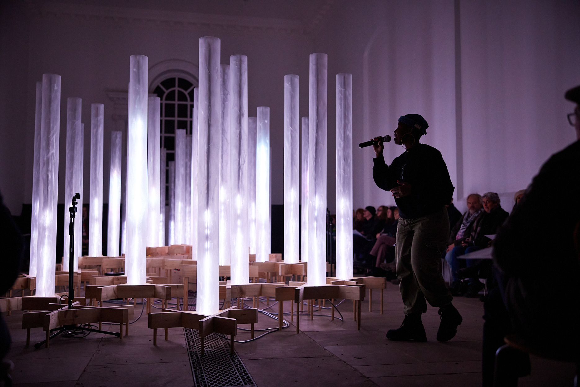 A woman singing into a microphone in front of a collection of white glowing columns