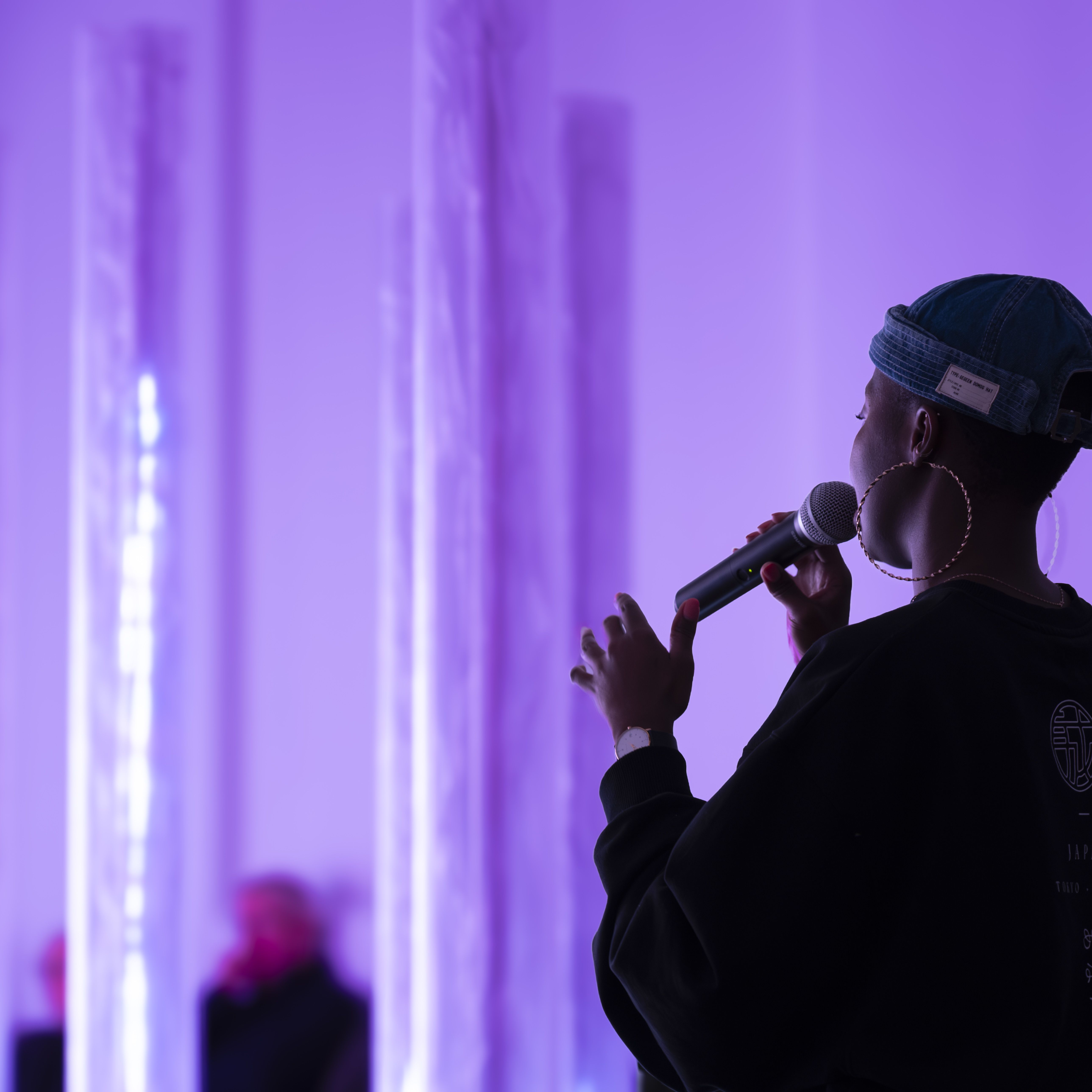 A woman singing into a microphone in front of a collection of purple glowing columns