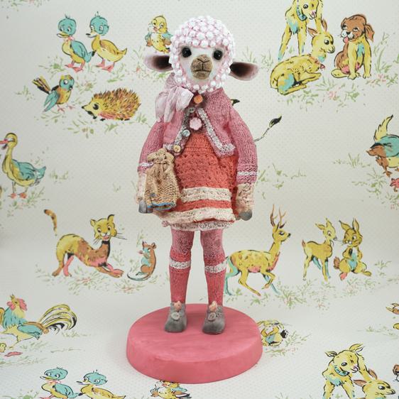 A pink toy sheep wearing a pink dress with a satchel across its shoulder