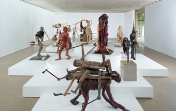 A display of human/animal figures on white plinths inside a gallery space.