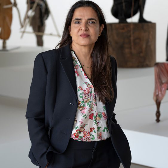 A woman wearing a black suit, standing in front of a display of humna/animal figures on plinths.