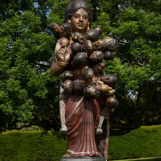 A sculpture of a giant Indian golu doll, with additional heads emerging from it's shoulders and torso, displayed outdoors.