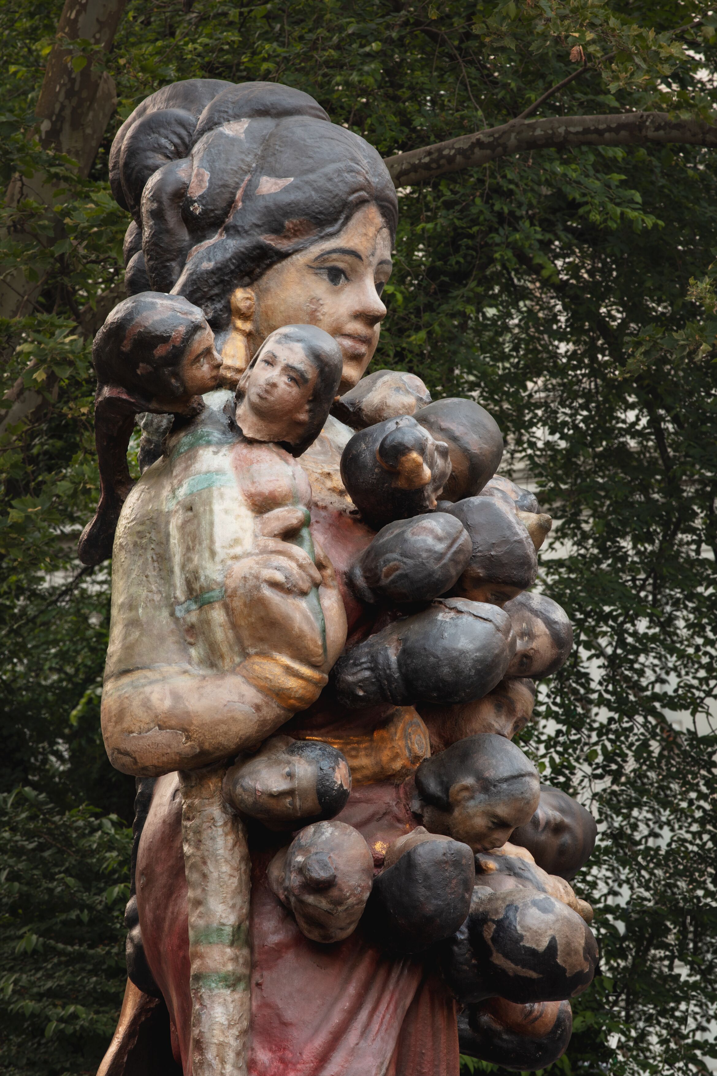 Sculpture of a female figure with multiple heads attached down her torso.
