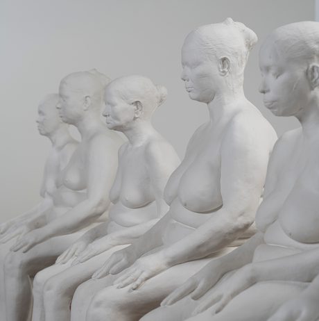 A row of white plaster casts of female seated nude figures.